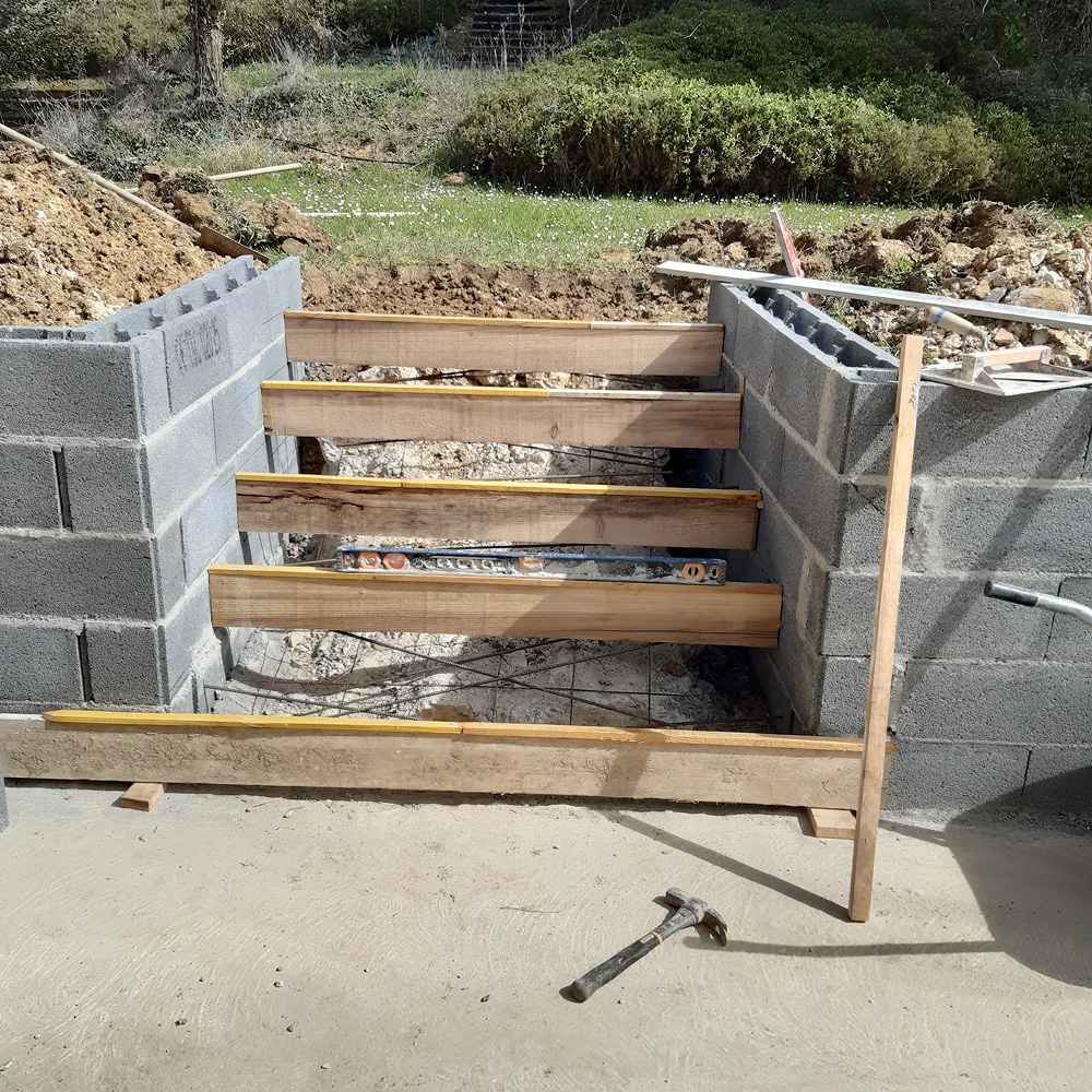 Construction d'escalier extérieur avec coffrage en bois Coffrage en bois pour construction d'escalier entre deux murs en parpaings avec ferraillage et niveau à bulle visible.