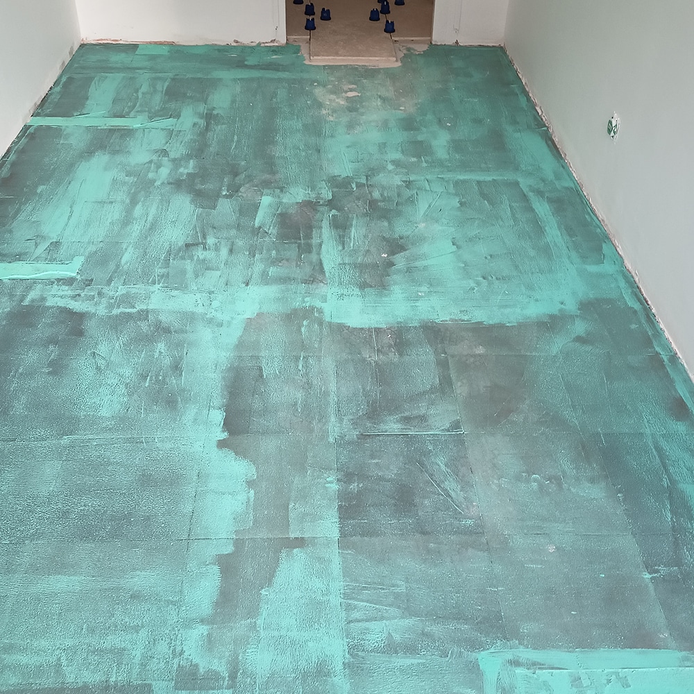 Étanchéité de sol avant carrelage : préparation rénovation Membrane d'étanchéité liquide turquoise sur un sol avant carrelage dans une pièce en rénovation.